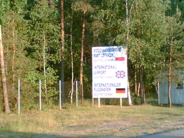 Dawne oznakowanie wjazdu na lotnisko w Szymanach; fotografia opublikowana pierwotnie w 2008 roku. Zdjęcie archiwalne, nie przedstawia obecnego wjazdu ani prac na DK57.