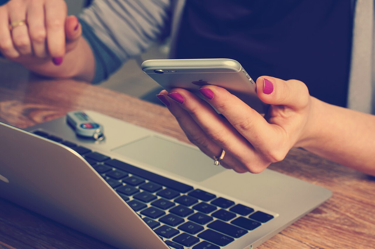 Korzystanie ze smartfona obok laptopa na fotografii Williama Ivena. Zdjęcie poglądowe do tematu pracy z narzędziami cyfrowymi; nie przedstawia uczestników zlotu MOK.